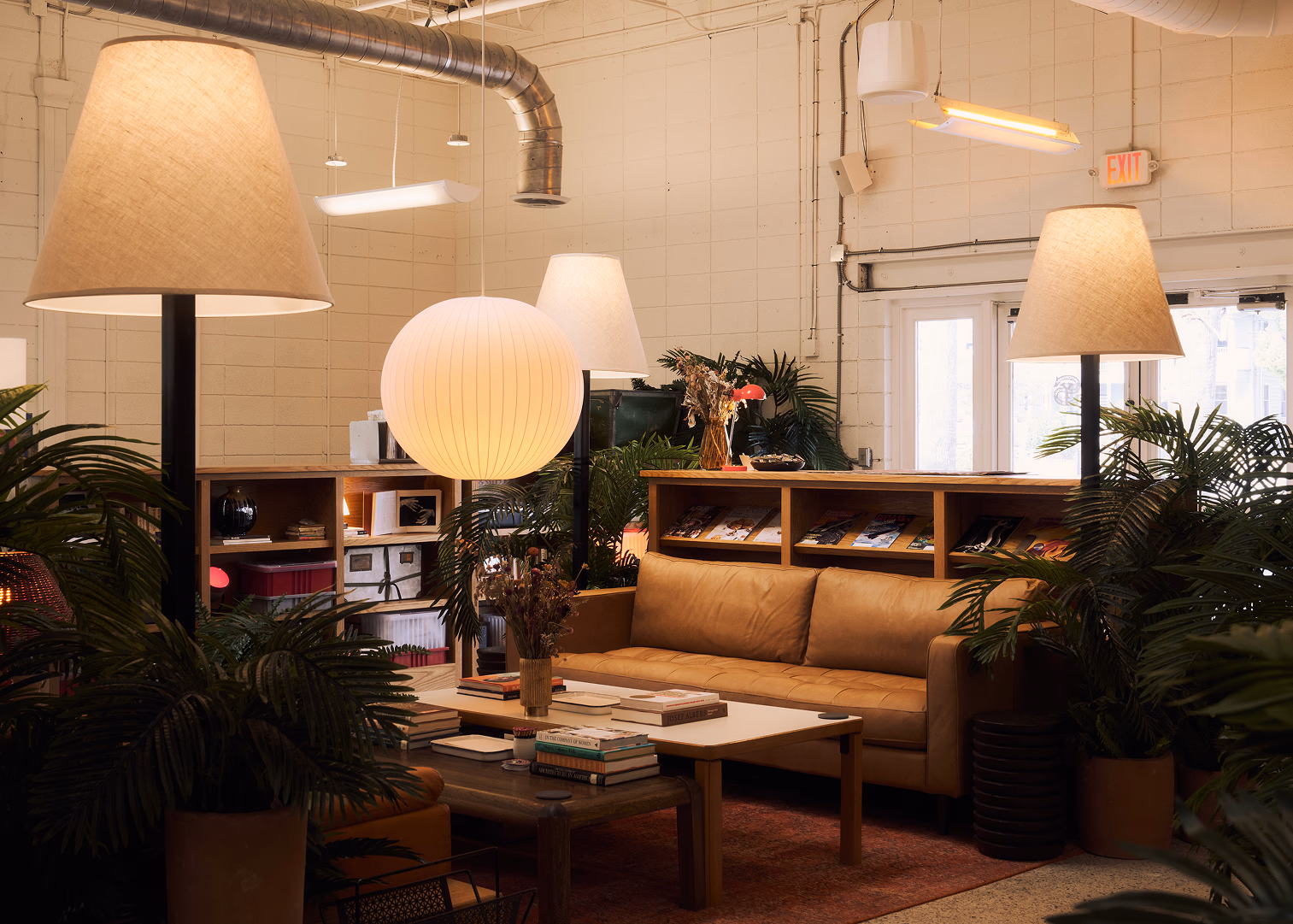 The Switchyards lounge on Rutledge Avenue: a tan leather sofa under paper pendant lamps, palms, and a ledge of magazines against a cream block wall.